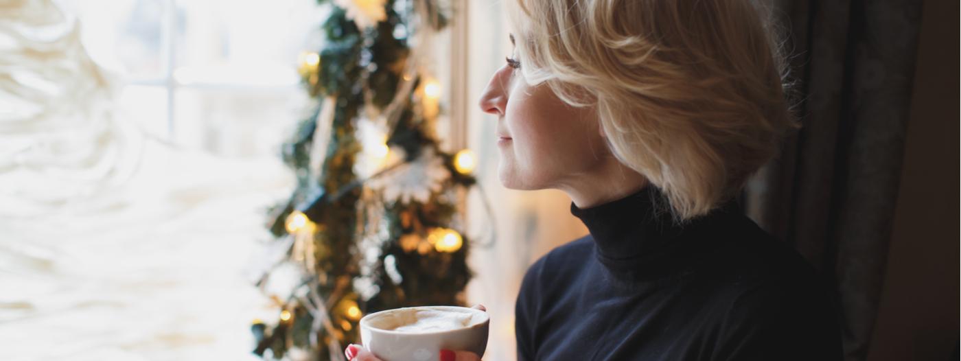 mladá žena dívající se z okna popíjí čaj. Vánoční dekorace.