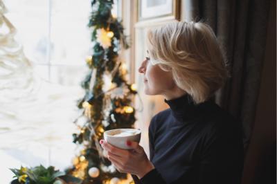 mladá žena dívající se z okna popíjí čaj. Vánoční dekorace.